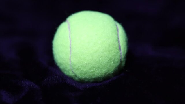 Una toma de cerca de una pelota de Tenis  con unas luces en un fondo negro