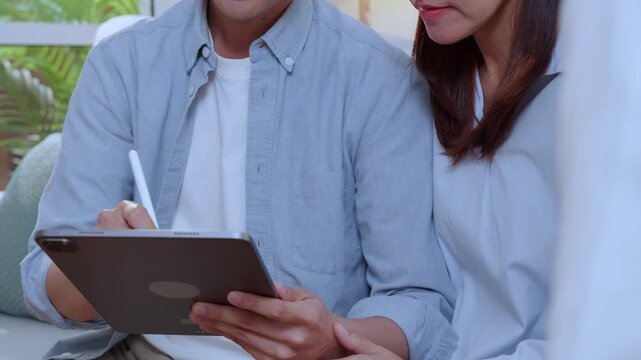 Asian couple signing digital contract on tablet screen during meeting, happy husband and wife signing electronic signature on tablet, clients approving digital insurance contract or investment.