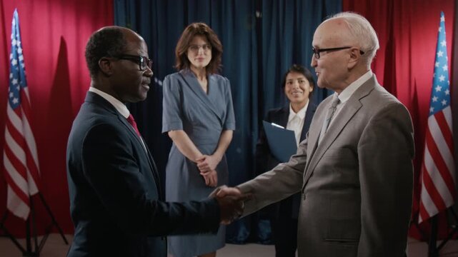 Two international diplomats shaking hands at summit with colleagues standing in background. Clip is ideal for political news and diplomatic broadcasts, side view shot