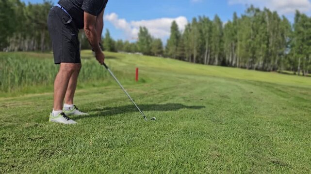 Golfer takes a swing on a sunny day at a green golf course with trees in the background