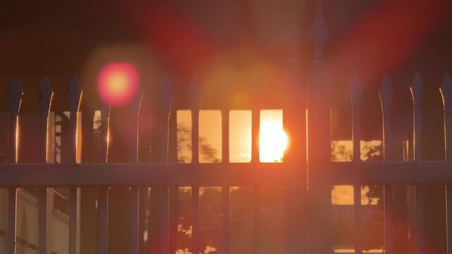 Golden sunset sunlight rays shining through metal security fence. Private property boundary concept