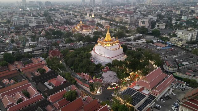 Aerial view of the golden stupa of Wat Saket temple surrounded by traditional rooftops and the urban skyline at dusk in Bangkok, Bangkok, Thailand.