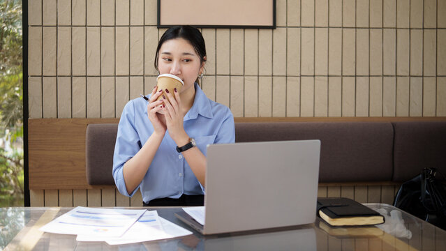 Businesswoman taking a coffee break while working on a laptop in a modern cafe workspace.