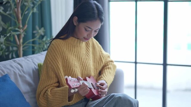Asian woman in sweater playing ukulele in living room