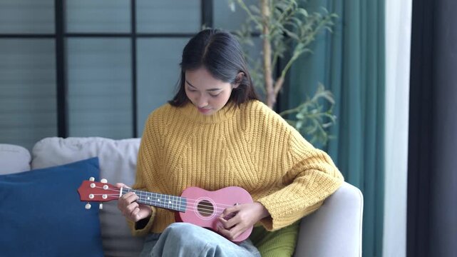 Asian woman in sweater playing ukulele in living room