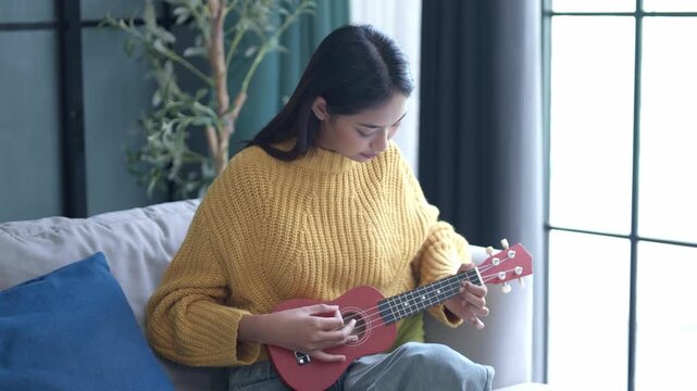 Asian woman in sweater playing ukulele in living room