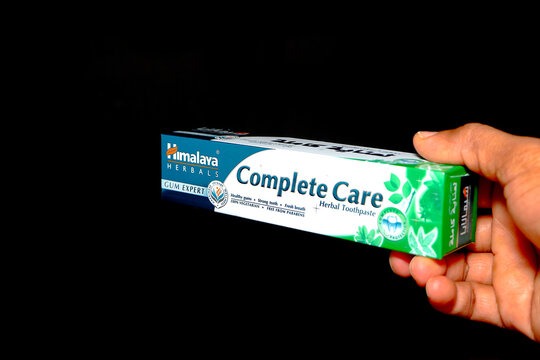 Himalaya complete care herbal toothpaste tube holding hand verticaly packaging against a black background closeup view.