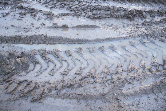 Close-up view of deep tire tread marks left in wet muddy ground. Detailed texture of soil deformation caused by heavy vehicle movement in off-road or construction conditions