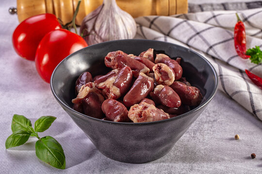 Raw chicken hearts in a bowl with fresh vegetables and herbs, preparation for a meal