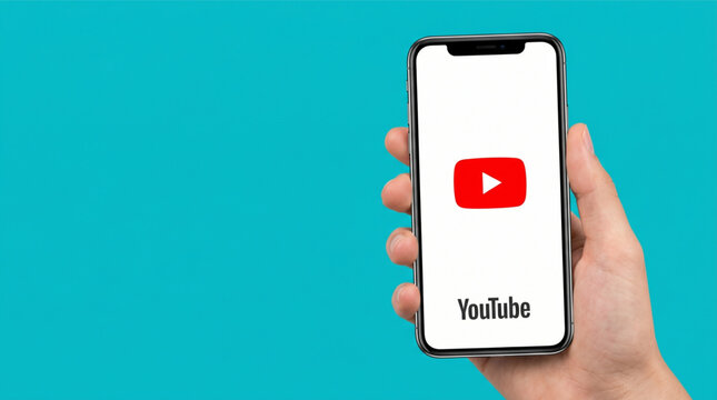 Male hand holding a smartphone iPhone with YouTube video sharing application logo on the white screen. Mobile device on teal background. Concept of social media, streaming and entertainment app.