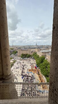 Aerial view of the Parvis Notre-Dame and the Paris skyline with the Eiffel Tower in the distance, framed between stone columns, showing tourists queueing to enter the famous landmark