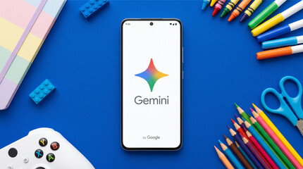 Fototapeta premium Google Gemini AI app on smartphone screen in a creative flat lay with school supplies, colored pencils, crayons, scissors, and a game controller on a vibrant blue background. Artificial intelligence.