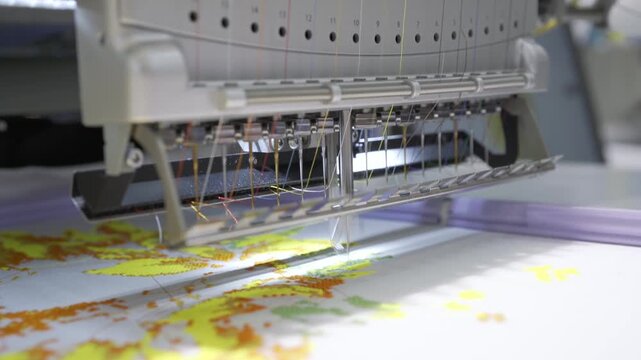 Industrial multi head embroidery machine working on fabric with complex colorful pattern and high precision needles.