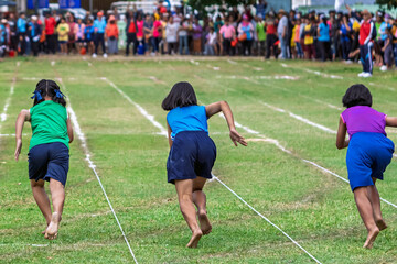 Barefoot school girls sprinting in running race at sports day. Back view of young schoolgirls running barefoot on field track, competing in sprint race during local community or school sports day.