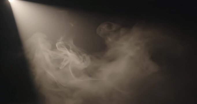 Soft, swirling smoke illuminated by a spotlight creating a dramatic atmosphere in a dark setting