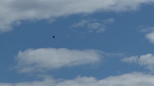 Mysterious Object in Blue Sky: A dark, unidentifiable object floats in a vast expanse of blue sky, partly obscured by fluffy white clouds.