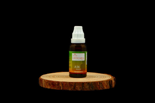 Allen - Urticaria drops A 56 medicine dropper bottle with  label and white cap resting on a rustic round wooden slice display stand for natural homeopathic health remedies on black background 