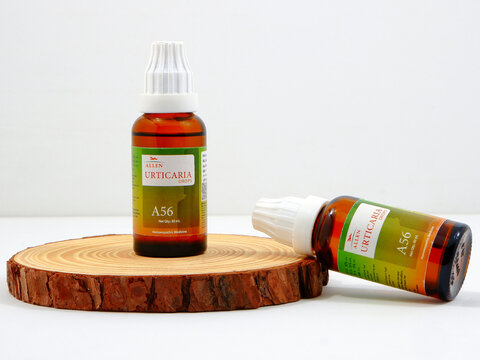 Allen - Urticaria drops A 56 medicine dropper bottles with  labels and white caps resting on a rustic round wooden slice display stand for natural homeopathic health remedies on white background 