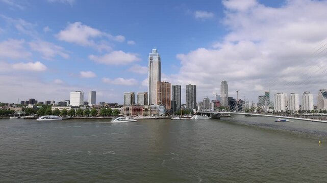 Aerial view of the Erasmusbrug bridge and modern skyscrapers along the Nieuwe Maas river with boats cruising the water in Rotterdam, Zuid-Holland, Netherlands.