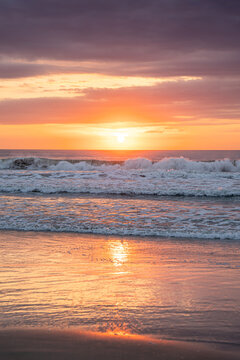Golden sun rising over ocean waves with a vibrant reflection on the wet sand. A vertical perspective of a beautiful morning on the beach in Corolla, North Carolina