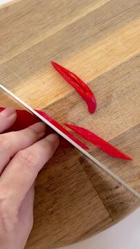 Red chili peppers are being chopped on a brown wooden cutting board.