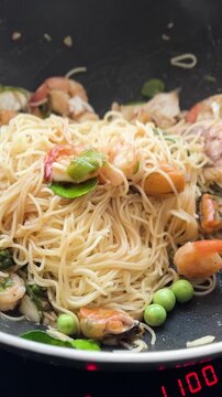 Spicy seafood spaghetti is simmering in a black pan, with smoke rising from the top.