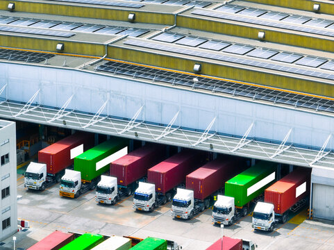 Solar-powered warehouse facility with freight trucks at loading docks. Eco-friendly logistics and efficient cargo transportation. Solar panels and sustainable energy concept in distribution center.