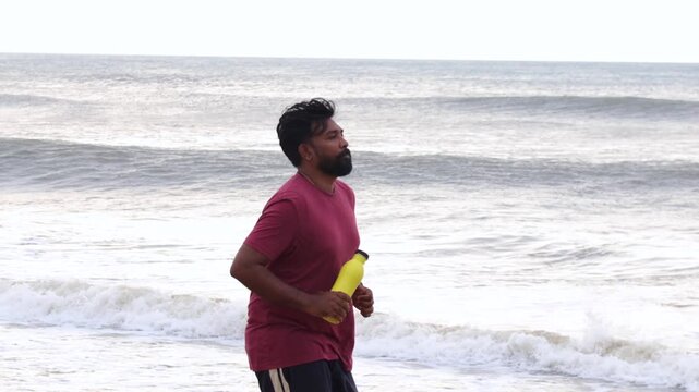 Bearded Man Jogging on Beach with Yellow Water Bottle for Summer Fitness and Hydration Lifestyle