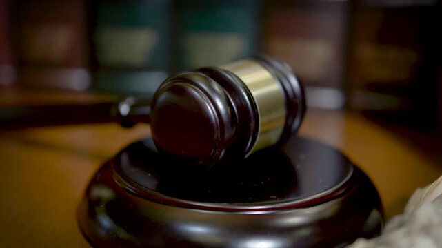 A judge's wooden gavel and sound block placed on a reflective wooden surface with a warm dark background in a legal setting.