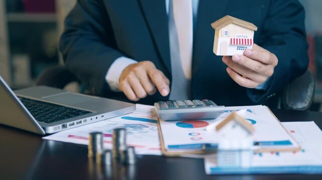 Businessman holding a coffee shop model while using a calculator to calculate business investment costs.