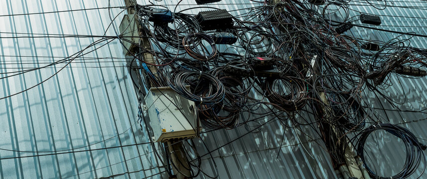 Tangled electrical wires and tangled communication lines on urban electric poles create a chaotic network. Disorganized and messy to organization management concept. Should take underground wire.