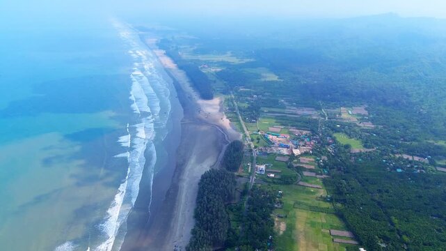 Aerial view of the expansive sandy beach and turquoise ocean waves meeting lush green hills and coastal settlements, Cox's Bazar, Chittagong Division, Bangladesh.