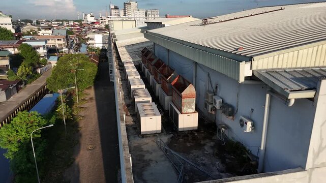 An aerial view captured by a drone shows large HVAC units on the roof and rusty ventilation ducts on a commercial building, with a cityscape in Indonesia in the background.