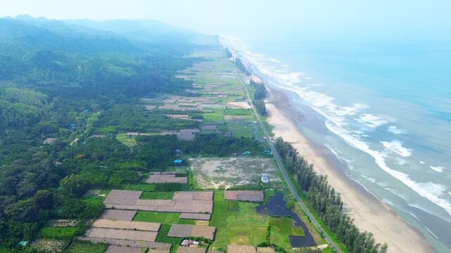 Aerial view of the long sandy beach and coastal road bordered by green agricultural plots and forested hills in Cox's Bazar, Chittagong Division, Bangladesh.