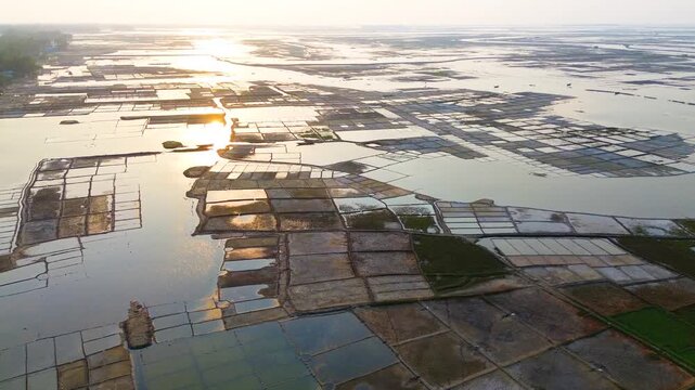 Aerial view of salt evaporation ponds with golden sunlight reflecting on the water surface at sunset in Cox's Bazar, Chittagong Division, Bangladesh.