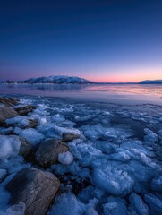 Fototapeta premium Sea ice and rocky shoreline at twilight along Norwegian fjord
