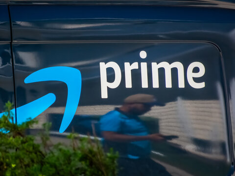 Calgary, Alberta, Canada. June 16, 2026. Close-up of Amazon Prime logo on a blue delivery van reflecting a courier checking his phone.