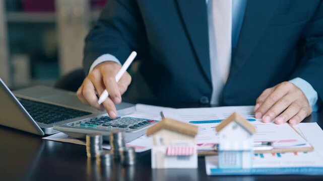Businessman analyzing financial charts, counting coins, and using a calculator to evaluate asset sales and profits.