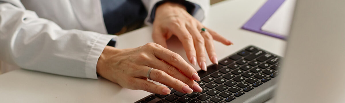 Header of doctor hands typing on computer during patient appointment, managing medical records. Useful for healthcare administration, clinic workflow marketing