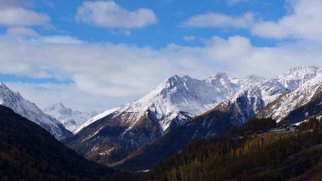 Aerial view of the snow-capped peaks and forested slopes of the Lower Engadine valley under a blue sky with scattered clouds in Bever, Grisons, Switzerland.