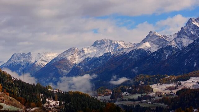 Aerial view of Schloss Tarasp nestled in the Engadin valley surrounded by snow-capped peaks and autumn forests in Scuol, Graubunden, Switzerland.
