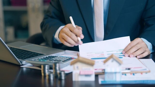 Businessman analyzing financial charts, counting coins, and using a calculator to evaluate asset sales and profits.