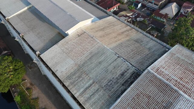 An aerial view of weathered corrugated metal warehouse roofs in an urban industrial area in Pontianak, Indonesia, captured by a drone.
