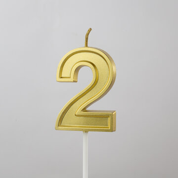 Gold number 2 birthday candle on grey  background