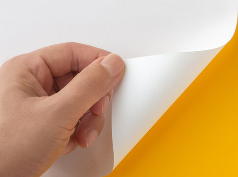 Close-up of hand peeling white paper corner to reveal yellow background mockup
