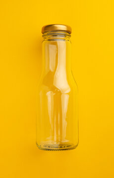 Empty Clear Glass Beverage Bottle with Gold Metal Lid on Bright Yellow Background