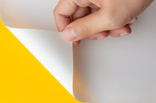Close-up of hand peeling white paper corner to reveal yellow background mockup
