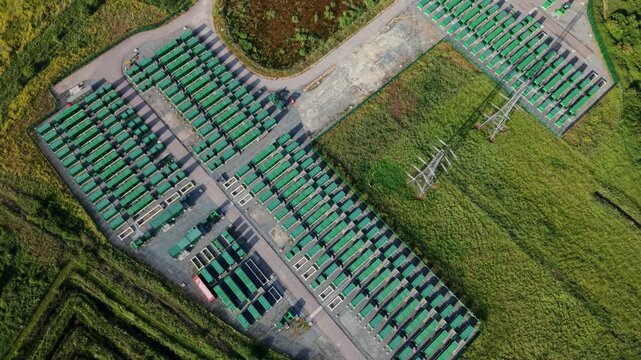 Aerial view of the Tilbury Battery Energy Storage System featuring rows of green battery units and electrical pylons in Tilbury, England, United Kingdom.