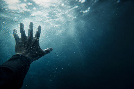 AI generated dramatic underwater view of hand reaching toward light through deep blue water bubbles conveying survival danger hope isolation human struggle