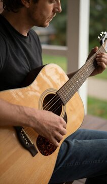 Man Engaged In Playing Acoustic Guitar Focused On Performance With Gaze Directed Downward Towards Instruments Fingerboard Subject Medium Length Hair